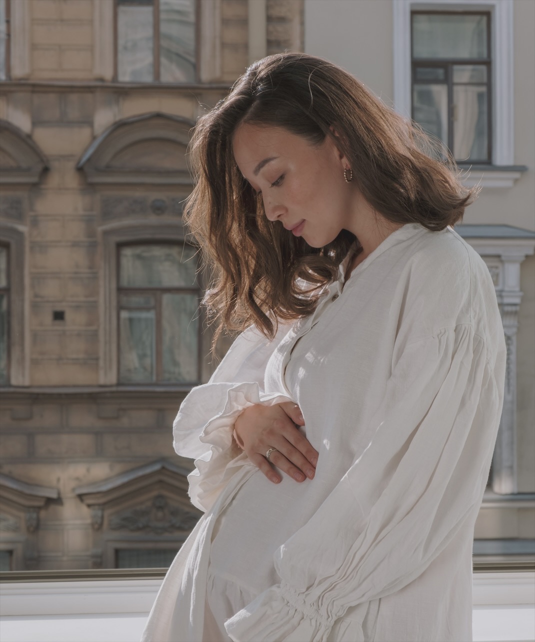 Бременна жена в ленена рокля с ръце върху корема